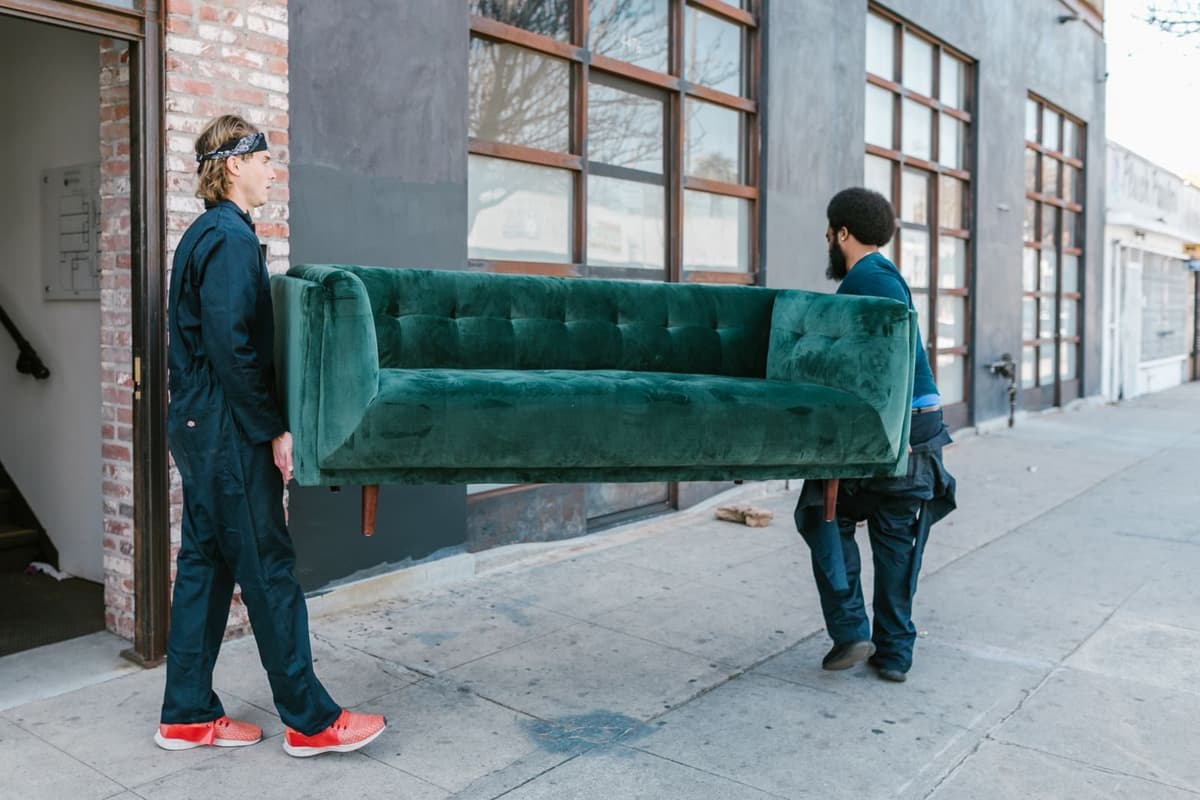 Two movers carrying a sofa out of a building onto the sidewalk